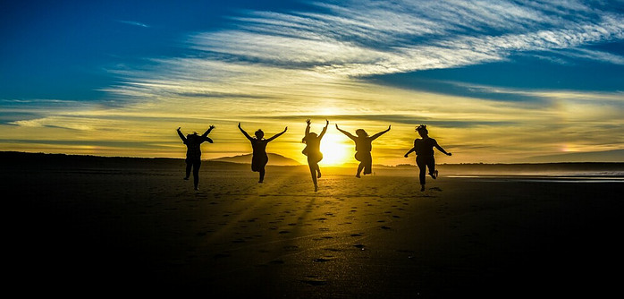 a group of people jumping in the air together in front of a sunset to celebrate their success.