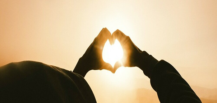 hands forming heart in front of the sunset to manifest love and abundance