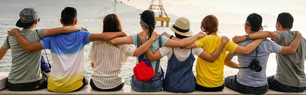a community of like minded individuals sitting side by side on a pier with arms over each others shoulders