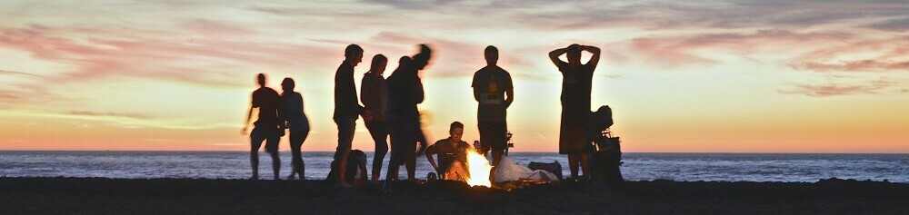 a group of people around a beach campfire at sunset to show a sense of community