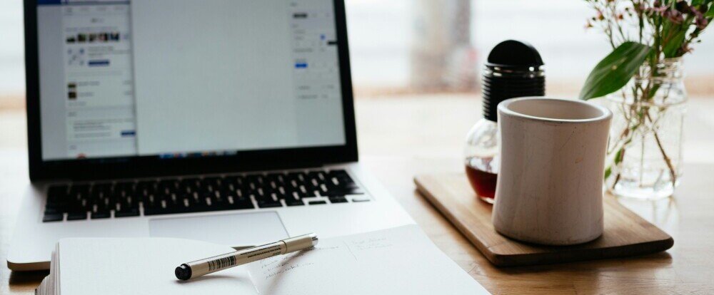 a notebook, laptop, coffee and flowers all set up for a day of content repurposing